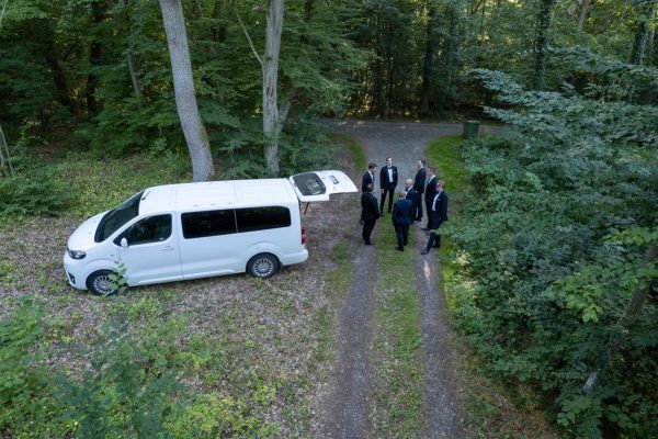 Drönarbild på Gosskören bakom en vit minibuss i skogen när de sjunger upp inför en 50 års fest